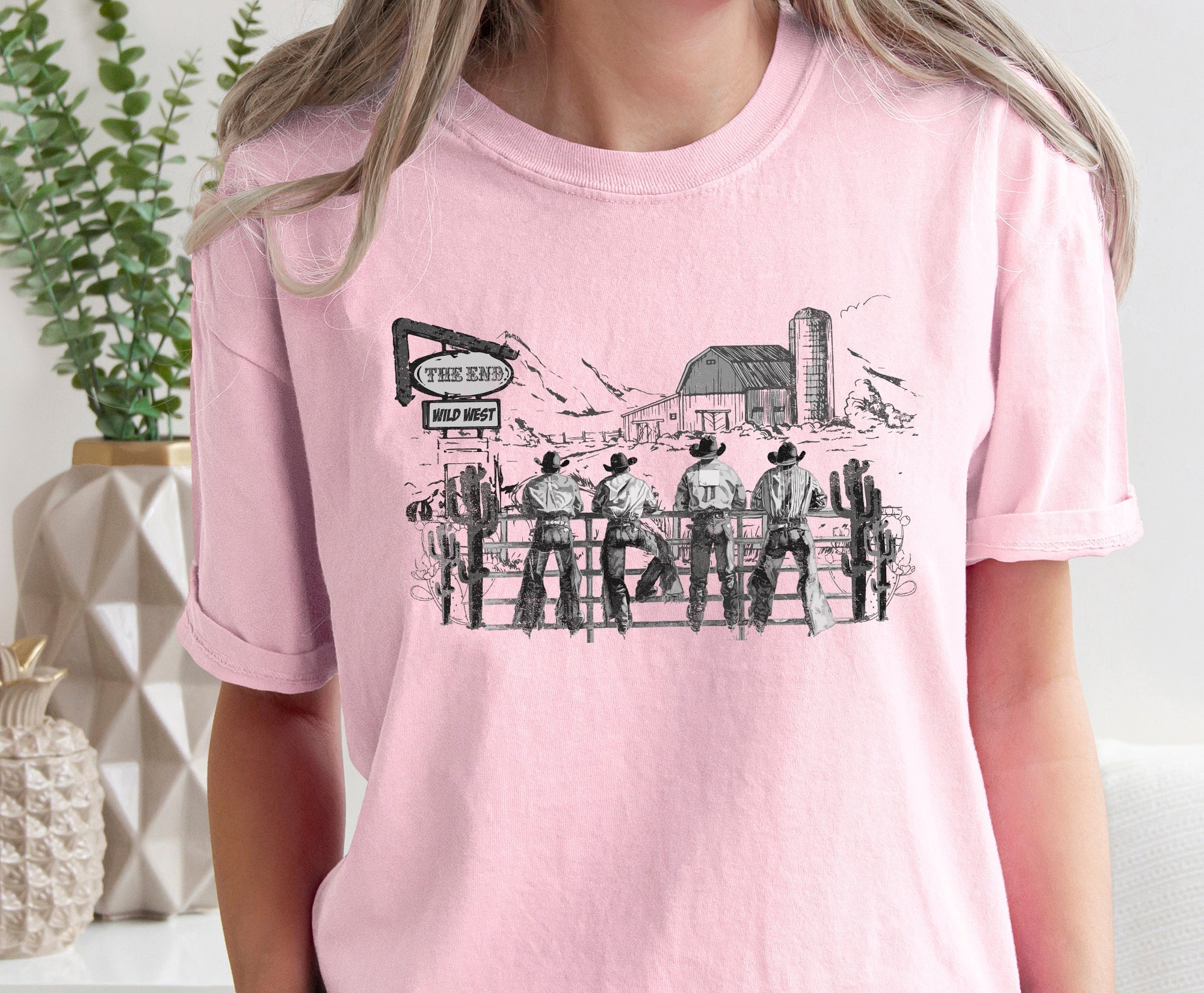 Person wearing a pink t-shirt with a graphic design of cowboys and a barn.